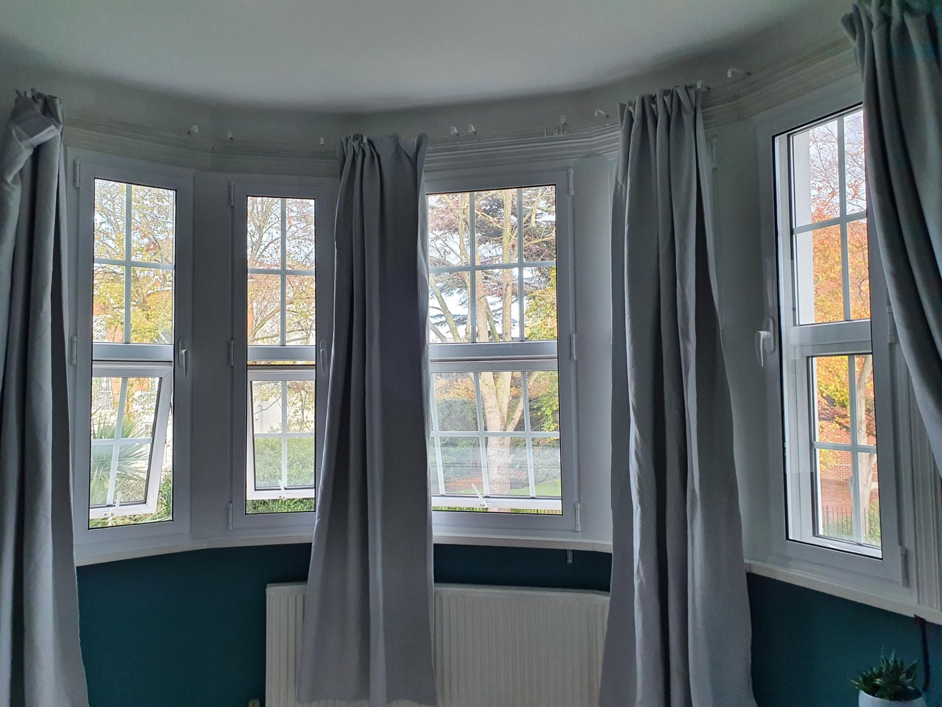 Bay and casement window combination featuring multiple tilt-and-turn windows with grey curtains, overlooking autumn trees